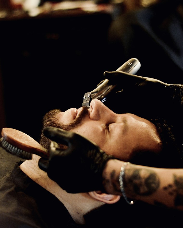 Barbeiro fazendo a barba de um cliente com navalha