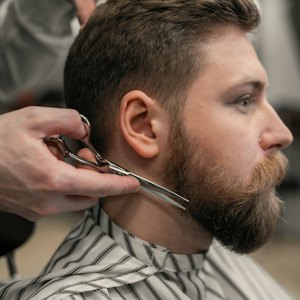 Barbeiro aparando a barba de um cliente com tesoura