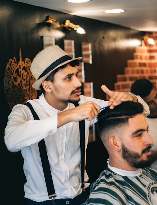 Barbeiro de chapéu finalizando um corte