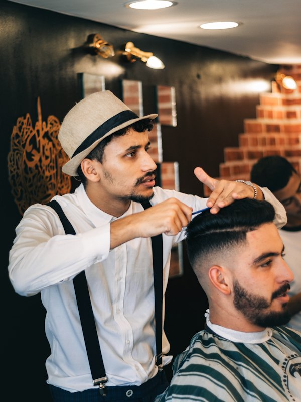 Barbeiro de chapéu finalizando um corte